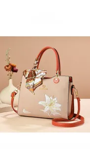 Détail de la broderie de lys sur sac à main beige avec poignée orange et foulard