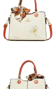 Détail de la broderie de lys sur un sac cabas crème avec des anses en cuir orange