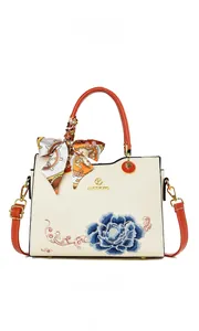 Detail of white leather handbag featuring blue peony embroidery and orange handle strap
