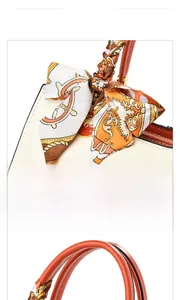 Detail of white leather handbag featuring orange handle and decorative vintage silk scarf
