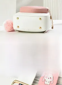 Detail of pink and white bag featuring golden metal feet and a decorative plush charm