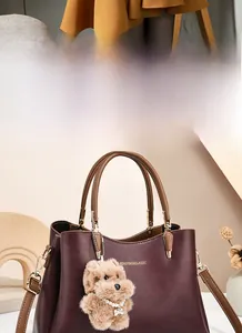 Detail of burgundy leather handbag featuring elegant handles and cute plush puppy charm
