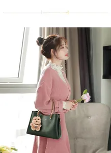 Detail of dark green tote bag with brown leather handles and plush bear charm accessory
