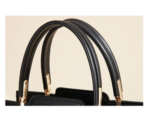 Detail of black leather handbag featuring dual handles and polished gold hardware accents