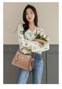 Brown leather tote bag with heart charm and golden logo held by a model with flowers
