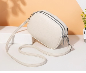 Detail of cream-colored cross-body bag with three zipper compartments and lychee pattern