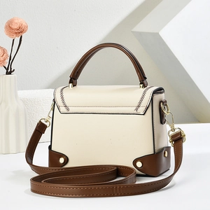 Elegant cream white box handbag with brown trim and gold hardware on a display stand
