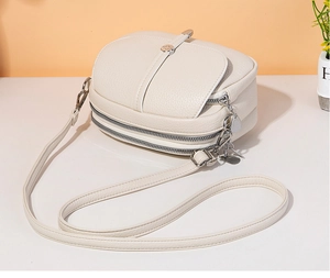 Detailed side view of cream faux leather crossbody bag featuring pebbled texture and zippers