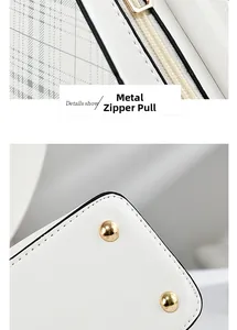 Detailed view of the metal zipper pull and golden protective studs on the white crossbody bag