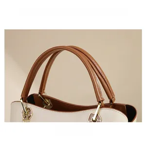 Close-up of brown leather handle and gold chain hardware on beige tote bag
