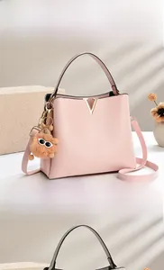 Detail of pink PU leather bucket bag with V-shaped metal logo and cute plush charm