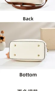 Detail view of white bucket bag featuring brown shoulder strap and protective gold metal feet
