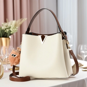 Elegant off-white PU leather bucket bag with gold V-detail and brown plush pendant