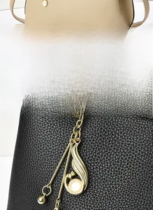Détail de sacs à main en cuir grainé avec pendentif plume dorée et décor de perle