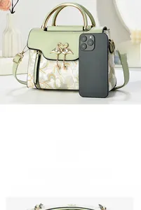 Detail of green leather handbag with floral print and crystal swan buckle near a phone