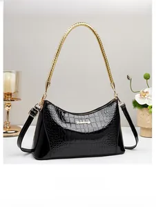 Detail of black glossy crocodile pattern handbag with golden woven handle and metal logo