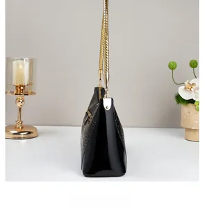 Detail view of black glossy crocodile texture leather handbag with golden chain handle