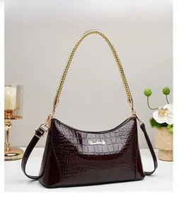 Detail view of coffee crocodile-patterned patent leather handbag with gold handle