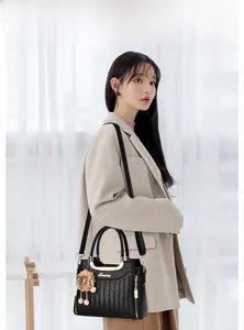 Detail of black woven leather handbag featuring gold metal handles and plush pompom charm