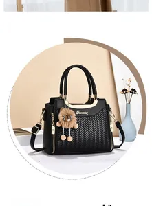 Detail of black tote with V-shaped woven texture, gold metal logo, and lion plush charm