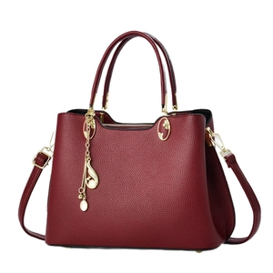 Sac à main bordeaux élégant avec motif litchi, détails dorés et pompon