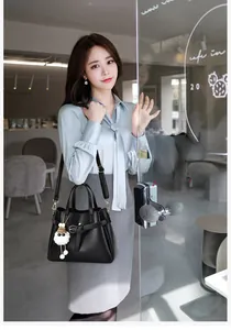 Close-up of black lychee texture leather handbag with white plush ball charm and strap
