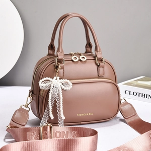 Detail of brown leather handbag featuring a pearl bow lace pendant and wide strap
