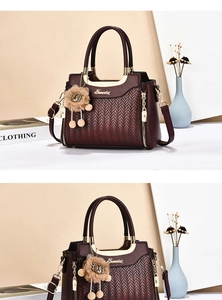 Detail of burgundy handbag with herringbone texture, gold handle and lion charm pendant