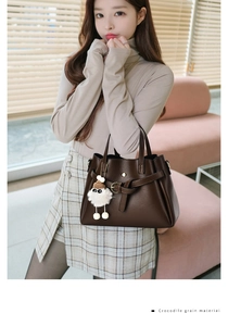 Detail view of deep brown handbag featuring refined crocodile grain texture and plush charm