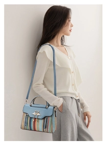 Close-up of blue leather flap bag with woven texture and gold swan clasp on a model