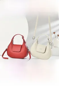Détail de sacs croissants rouge et crème avec texture cuir grainé et finitions métal
