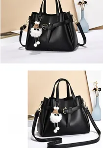 Detail of black pebbled leather handbag with gold hardware and white plush charm accessory
