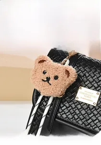 Close-up of a plush khaki bear charm with golden clip on a black woven texture bag