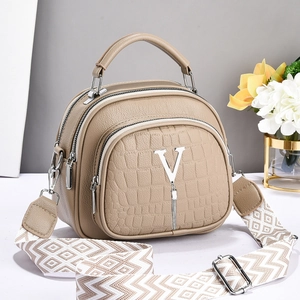 Detail of khaki crocodile texture handbag with metal V logo and tassel ornament