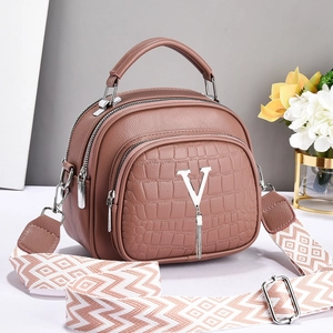 Detail of dust pink handbag showing triple-zipper design and geometric woven strap