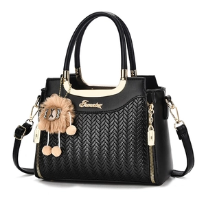 Black herringbone handbag with gold metal handles and a plush bear charm on white background