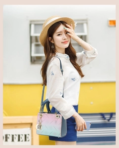 Detail of pink and blue gradient handbag with gold metal logo charm in sunny outdoor setting