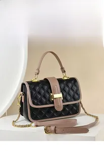 Detail of black quilted chain bag with beige piping and gold metal clasp on a white stand