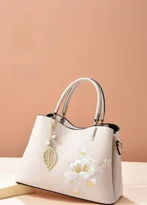 Detail of cream handbag with elegant floral embroidery and pearl leaf pendant accent