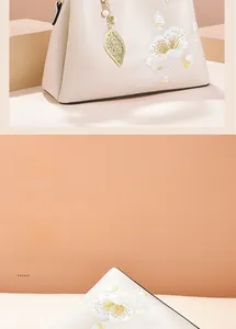 Close-up of elegant floral embroidery and golden leaf charm on beige handbag