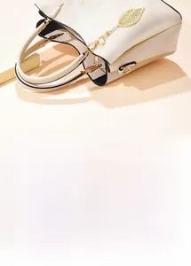 Detail of cream faux leather handbag with golden leaf pendant and pearl decoration