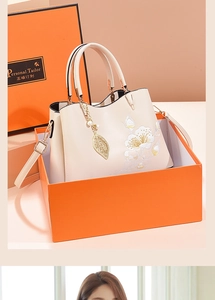 Detail of beige leather handbag featuring floral embroidery and elegant pearl charm
