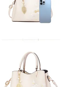 Detail of cream luxury handbag with floral embroidery and gold leaf pearl charm