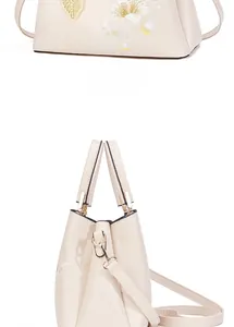 Detailed embroidery of white flowers and golden leaf charm on beige luxury handbag