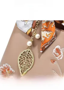 Détail d'un sac à main brodé avec pendentif feuille dorée, perles et foulard en soie