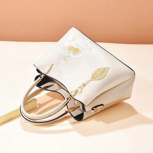 Elegant beige tote bag with yellow floral embroidery and pearl leaf charm accessory