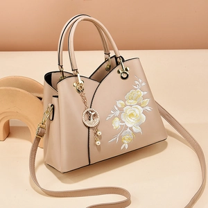 Beige tote bag with floral embroidery and golden fish pendant on minimalist background