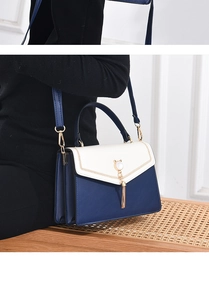 Detail of a navy and cream crossbody bag featuring a pearl cat-ear charm and golden tassels