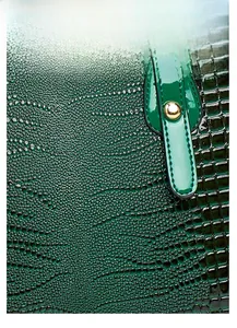 Detail of dark green synthetic leather featuring crocodile texture and gold hardware