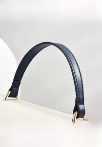 Detail of blue leather handle with gold ring connector on a cream crossbody bag